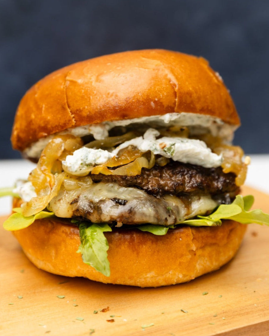 A smash burger with tarragon and black truffle, served in a toasted brioche bun with visible layers of meat, cheese, and vegetables.